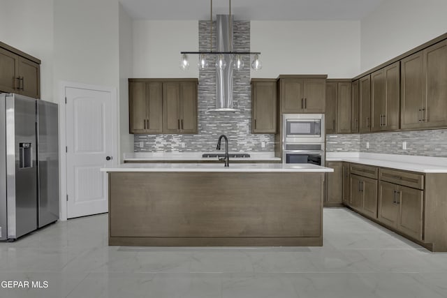 kitchen featuring hanging light fixtures, an island with sink, stainless steel appliances, and a towering ceiling