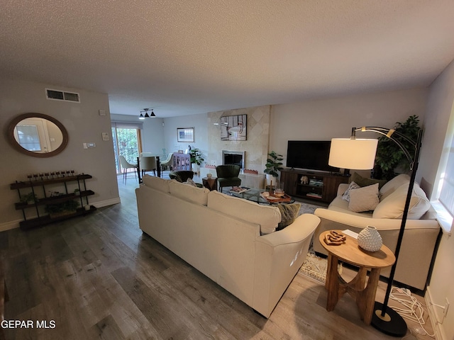 living room with a tiled fireplace, a textured ceiling, and hardwood / wood-style floors