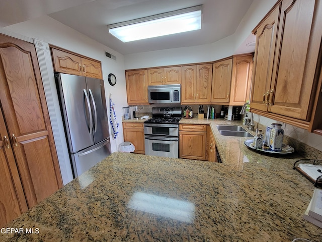 kitchen featuring light stone counters, stainless steel appliances, and sink