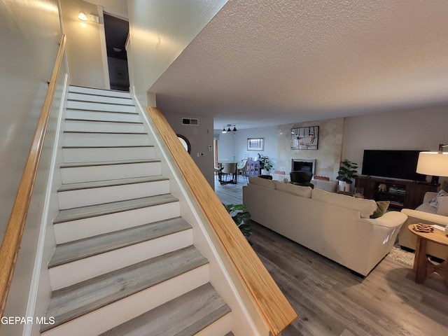 staircase with wood-type flooring, a textured ceiling, and a tile fireplace