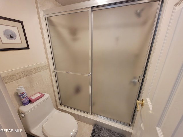 bathroom with a shower with door, toilet, and tile walls