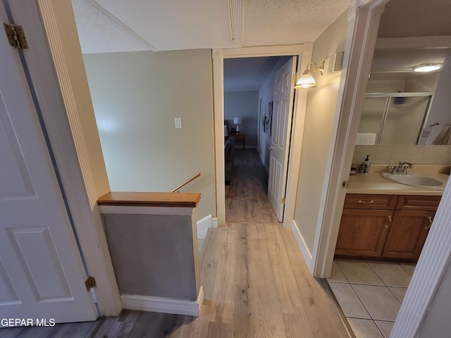 corridor with light hardwood / wood-style floors, a textured ceiling, and sink