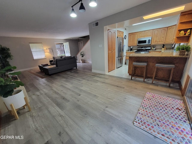 interior space featuring appliances with stainless steel finishes, kitchen peninsula, light wood-type flooring, and a breakfast bar