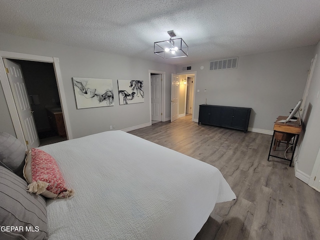 bedroom with ensuite bathroom, wood-type flooring, a textured ceiling, and a chandelier