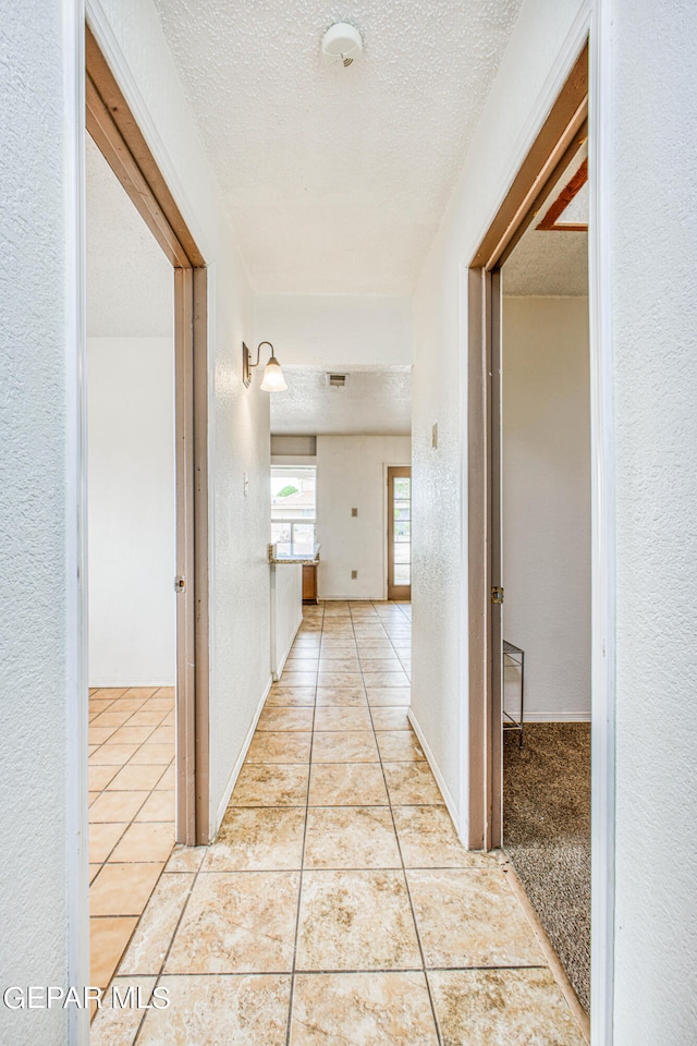 hall with a textured ceiling and light tile patterned flooring