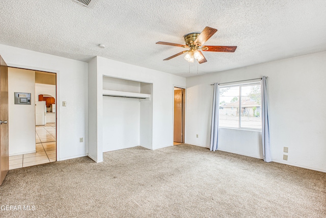 unfurnished bedroom with a textured ceiling, carpet floors, a closet, ceiling fan, and white refrigerator