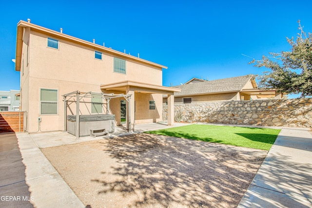 back of house with a hot tub, a patio area, and a lawn