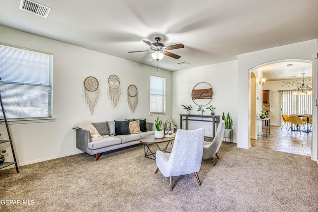 carpeted living room with ceiling fan with notable chandelier