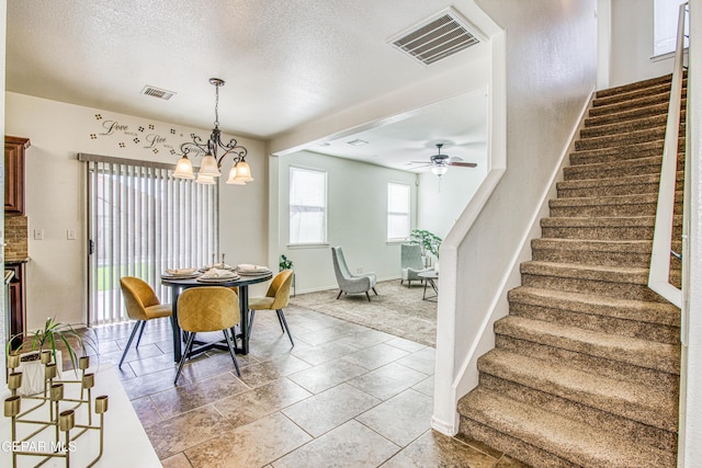 tiled dining area featuring ceiling fan with notable chandelier and a textured ceiling