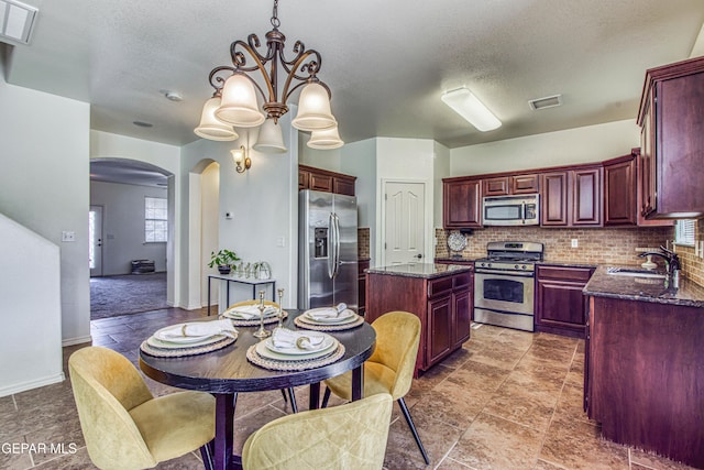 kitchen featuring sink, decorative backsplash, a kitchen island, stainless steel appliances, and a chandelier