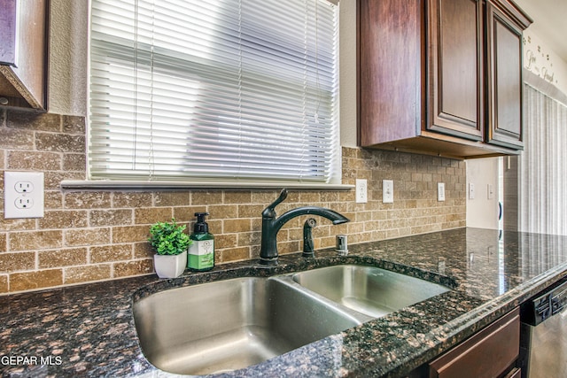 kitchen with stainless steel dishwasher, sink, dark stone counters, and tasteful backsplash