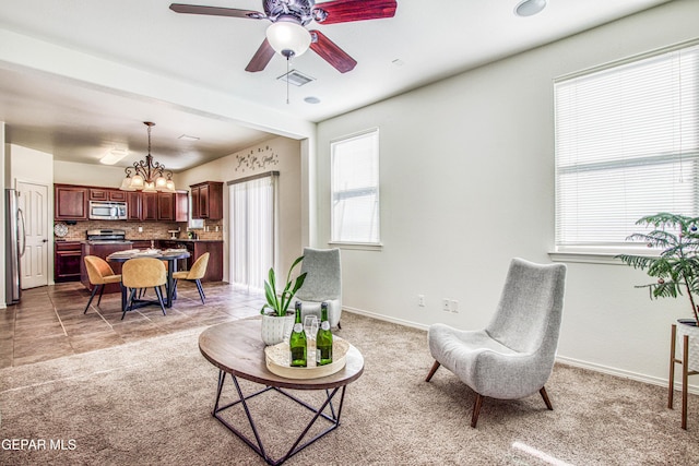 sitting room with beamed ceiling, light colored carpet, and ceiling fan with notable chandelier