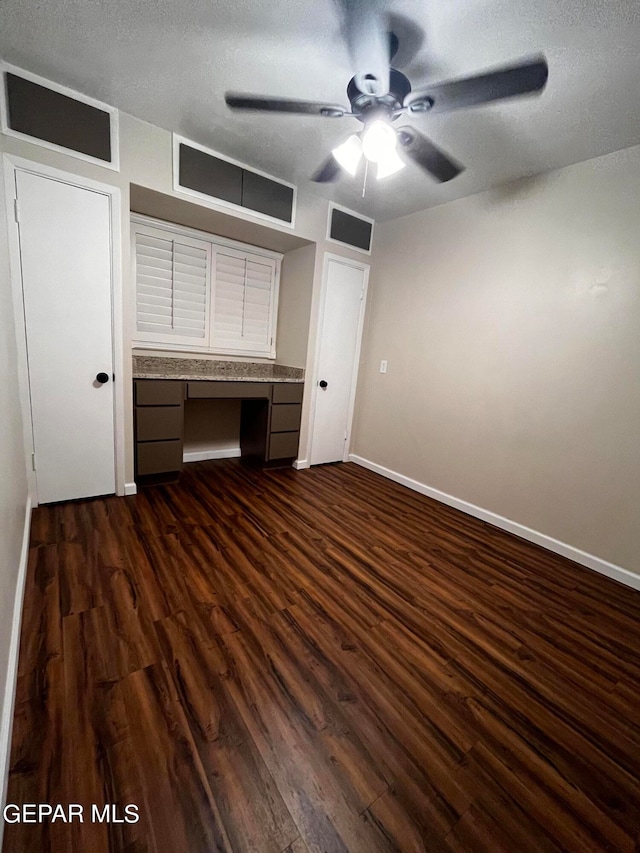 unfurnished bedroom featuring ceiling fan, dark hardwood / wood-style flooring, built in desk, and a textured ceiling