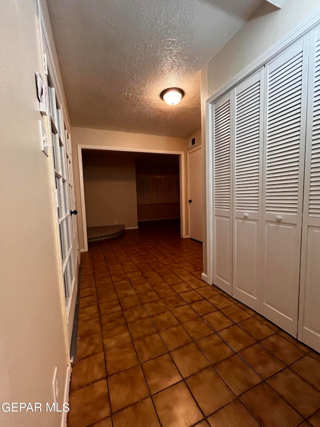 corridor featuring dark tile patterned floors and a textured ceiling