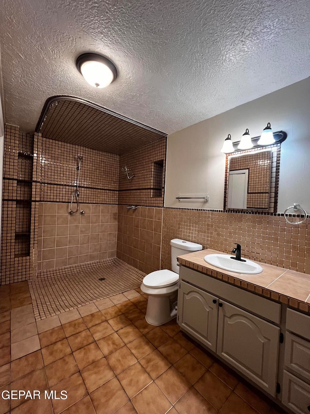 bathroom with toilet, tile walls, a textured ceiling, a tile shower, and vanity