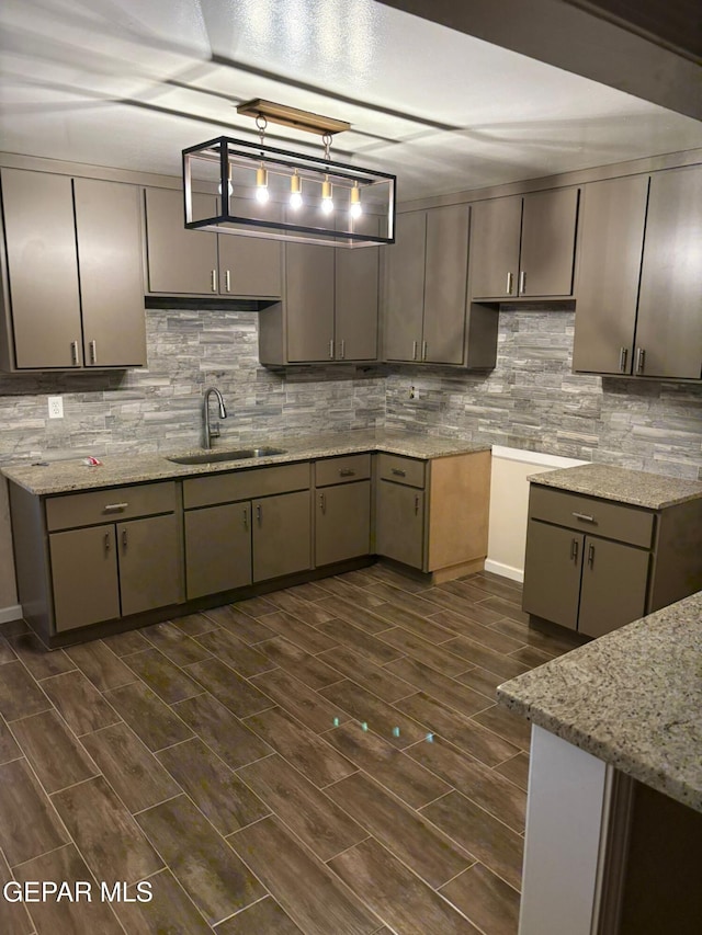 kitchen featuring hanging light fixtures, backsplash, light stone countertops, and sink