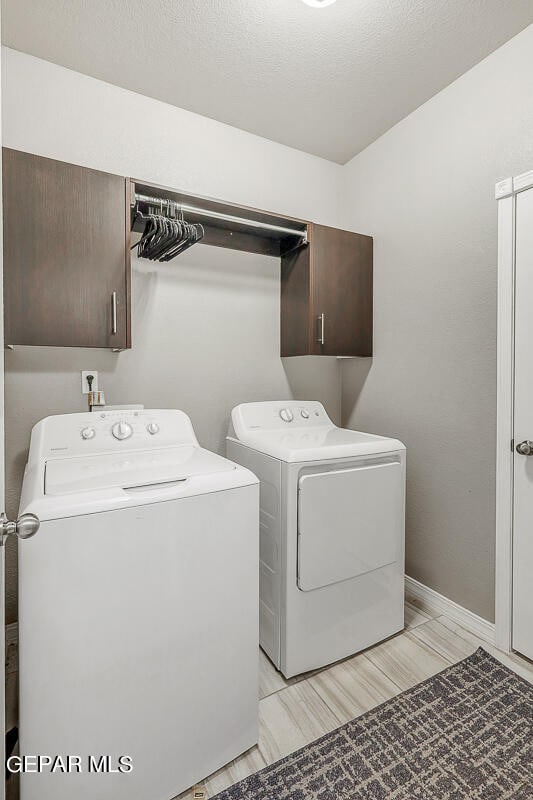 washroom featuring cabinets, light hardwood / wood-style flooring, a textured ceiling, and washing machine and clothes dryer