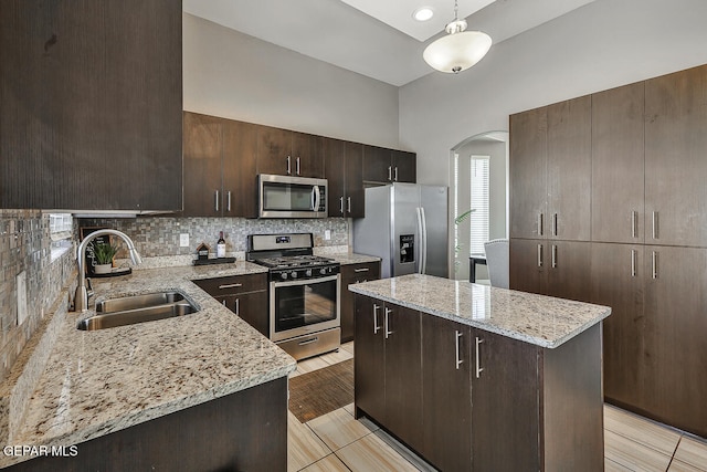 kitchen with sink, a kitchen island, stainless steel appliances, dark brown cabinetry, and light stone counters