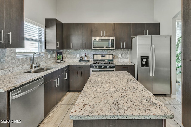 kitchen featuring decorative backsplash, a kitchen island, appliances with stainless steel finishes, light stone countertops, and sink