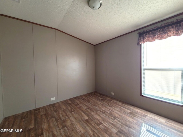 unfurnished room featuring ornamental molding, lofted ceiling, a textured ceiling, and hardwood / wood-style flooring