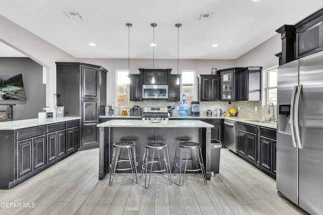 kitchen with appliances with stainless steel finishes, light wood-type flooring, a center island, a kitchen breakfast bar, and decorative light fixtures