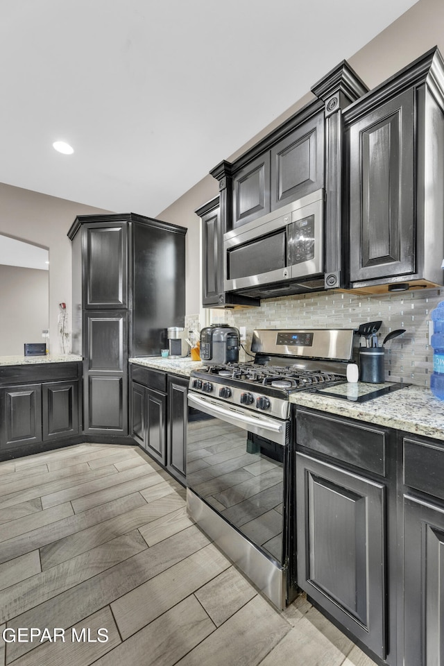 kitchen with backsplash, light stone countertops, stainless steel appliances, and light wood-type flooring