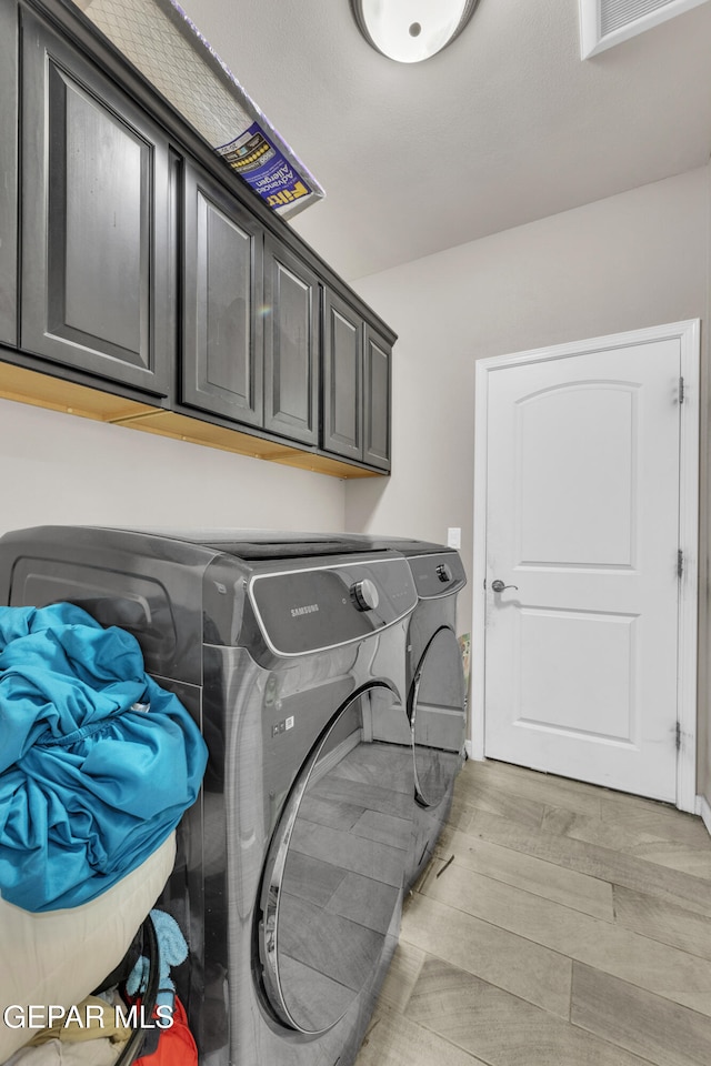 clothes washing area with independent washer and dryer, light hardwood / wood-style floors, and cabinets