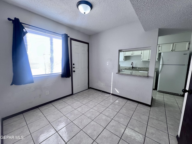 interior space featuring white cabinetry, sink, white fridge, a textured ceiling, and light tile patterned flooring