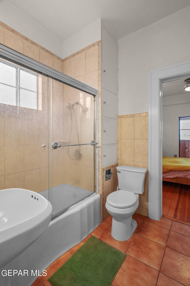 bathroom with toilet, tile walls, tile patterned floors, and shower / bath combination with glass door