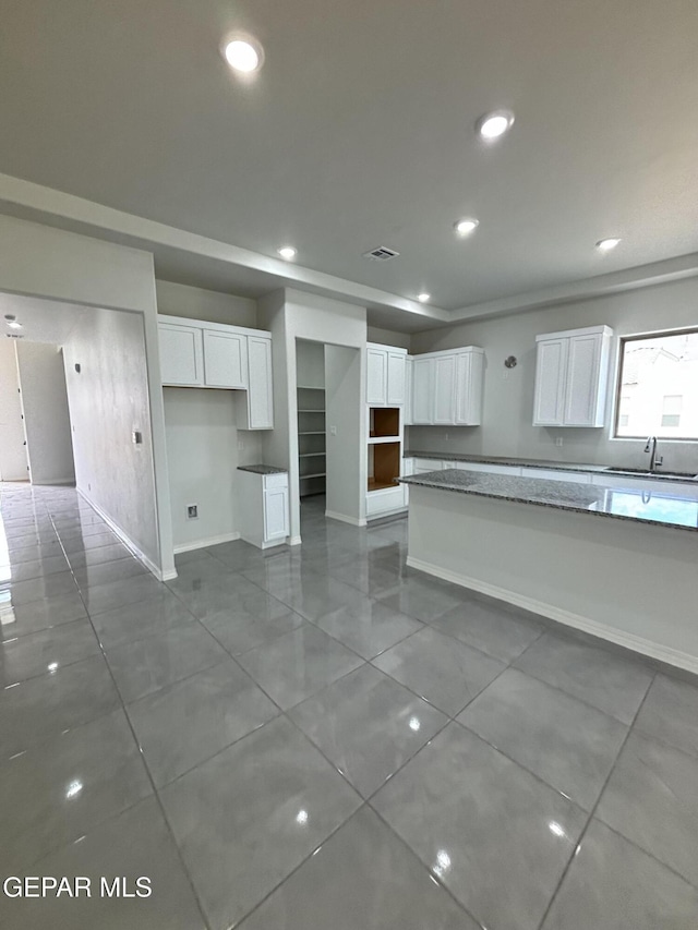 kitchen featuring baseboards, visible vents, recessed lighting, a sink, and white cabinetry