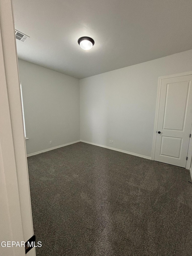 spare room with visible vents, dark carpet, and baseboards