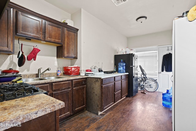 kitchen with dark brown cabinets, sink, black refrigerator, and dark hardwood / wood-style flooring