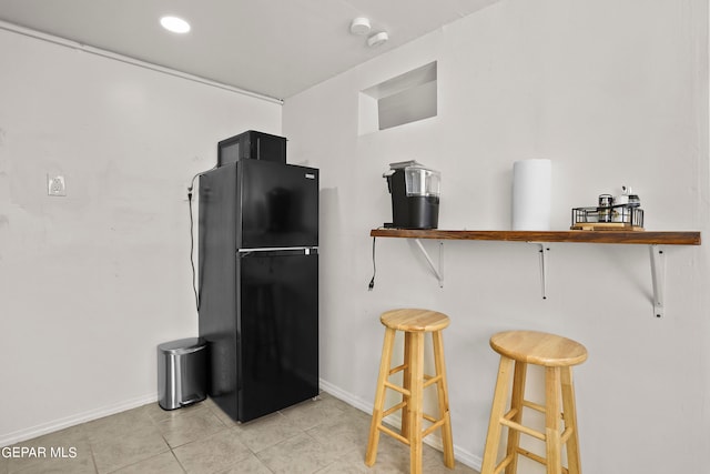 kitchen featuring a breakfast bar area, light tile patterned floors, and black fridge