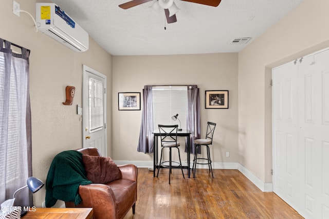 living area featuring a textured ceiling, hardwood / wood-style floors, an AC wall unit, and ceiling fan