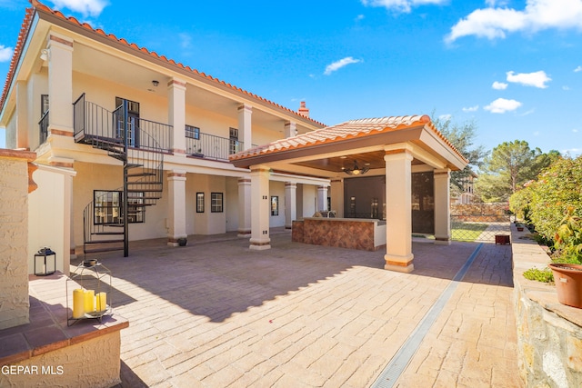 rear view of property with ceiling fan, a balcony, and a patio area