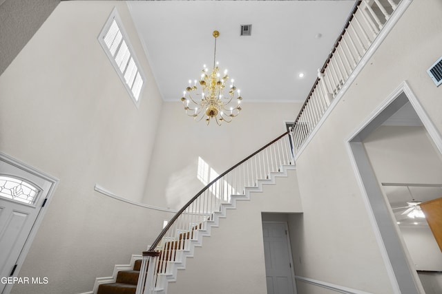 stairs with ornamental molding, a high ceiling, and an inviting chandelier