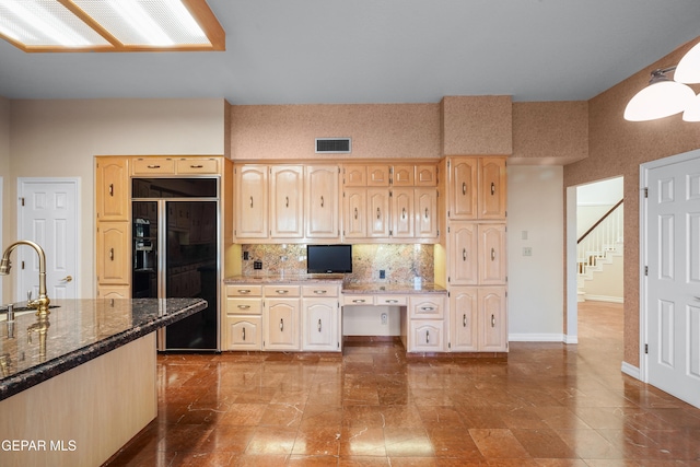 kitchen with black fridge, built in desk, decorative backsplash, sink, and dark stone countertops