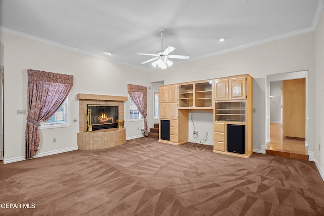 unfurnished living room with ceiling fan, a tiled fireplace, crown molding, and carpet