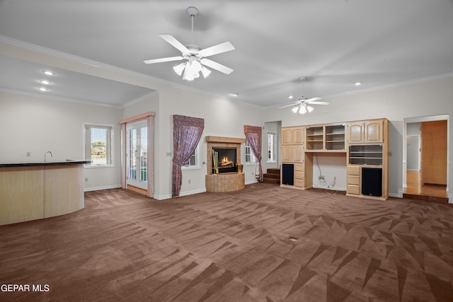 unfurnished living room with ceiling fan, dark colored carpet, and ornamental molding