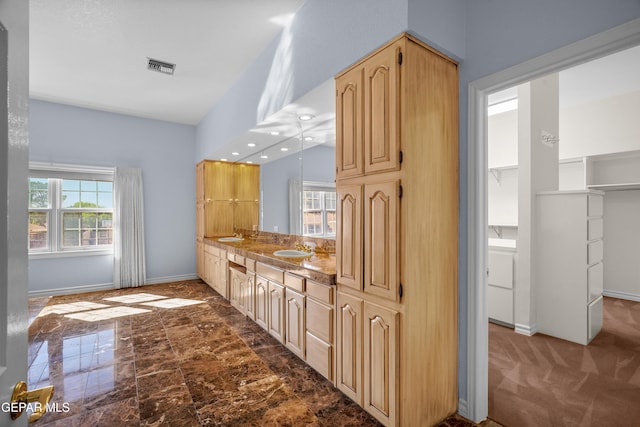 kitchen with light brown cabinetry, light stone counters, sink, and carpet flooring