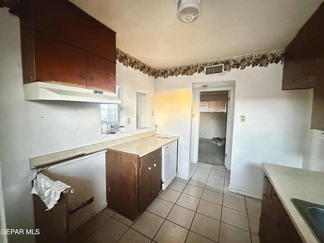 kitchen featuring white dishwasher, light tile patterned floors, dark brown cabinetry, and sink