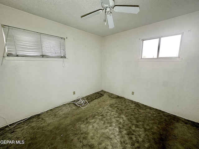 empty room featuring ceiling fan, a textured ceiling, and dark colored carpet