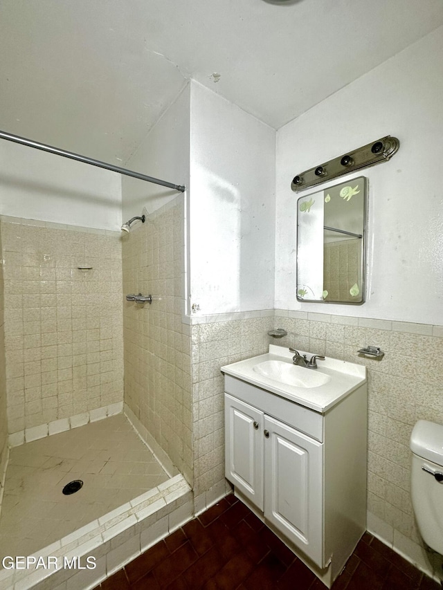 bathroom with a tile shower, tile walls, vanity, and toilet