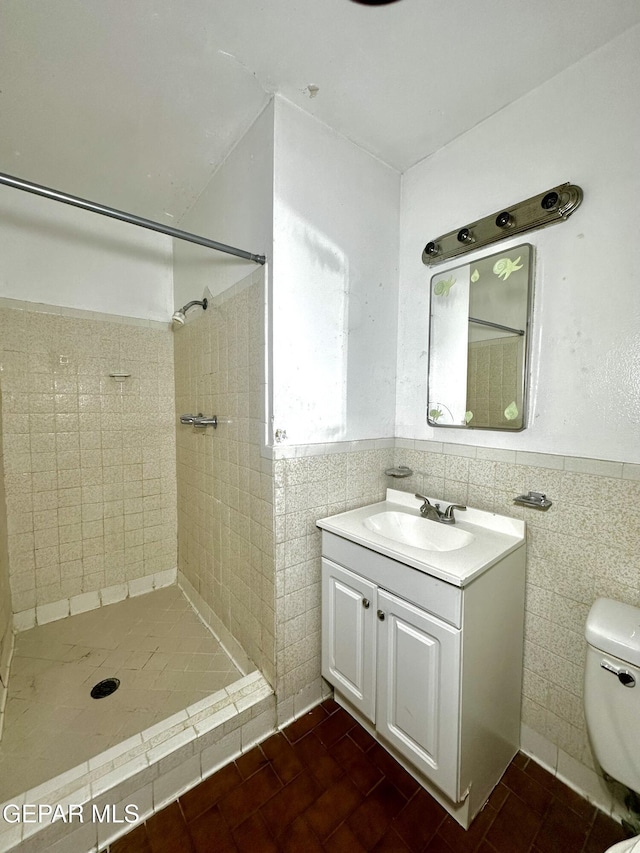 bathroom with tiled shower, vanity, toilet, and tile walls