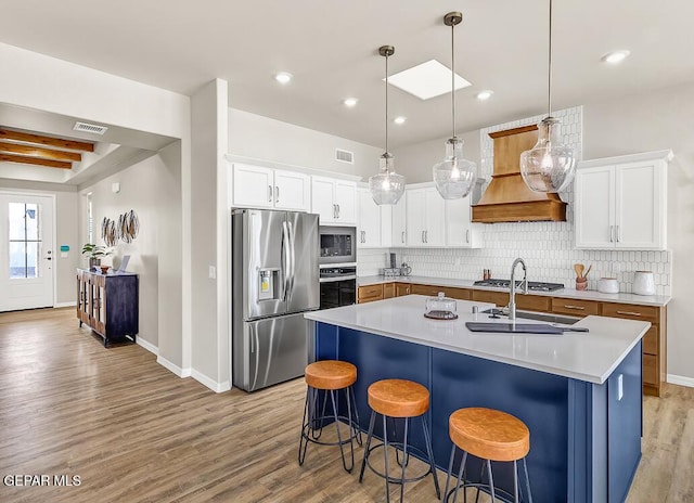 kitchen featuring white cabinetry, appliances with stainless steel finishes, an island with sink, and custom range hood