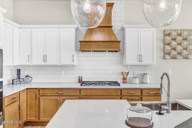 kitchen featuring backsplash, stainless steel gas cooktop, custom range hood, and white cabinets