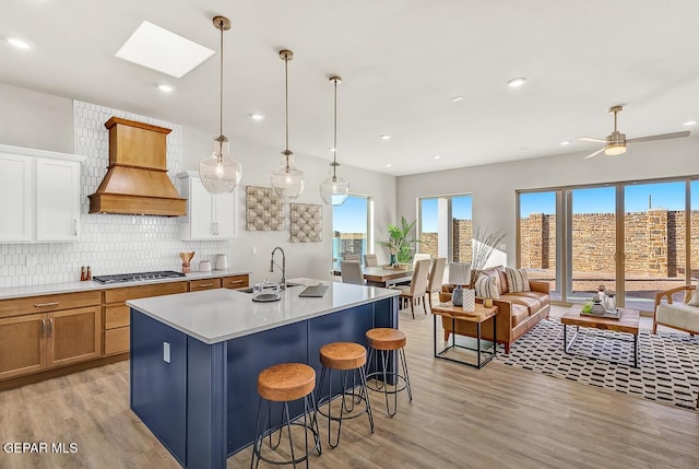 kitchen featuring premium range hood, a center island with sink, pendant lighting, stainless steel gas stovetop, and backsplash