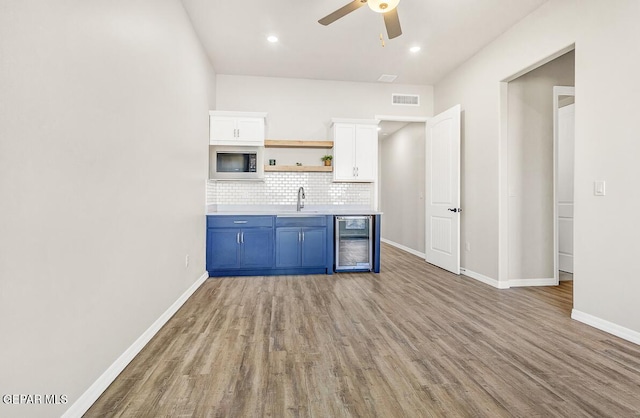 kitchen with white cabinets, beverage cooler, backsplash, and light hardwood / wood-style flooring