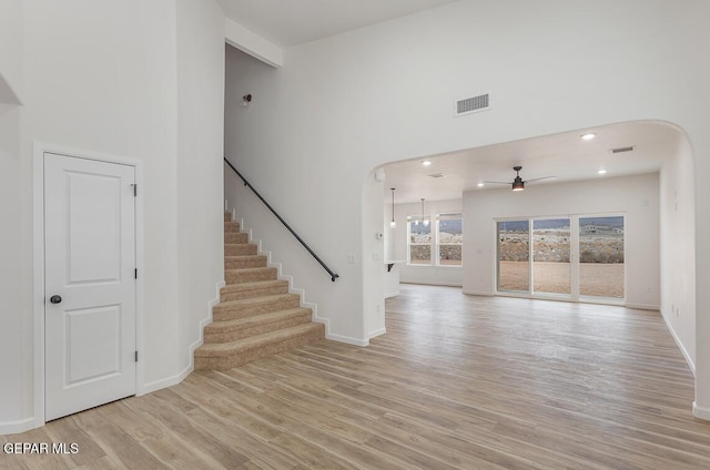 unfurnished living room featuring ceiling fan, light hardwood / wood-style floors, and a high ceiling