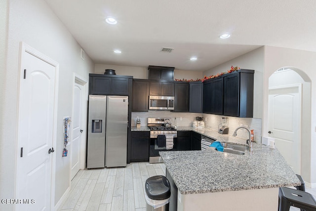 kitchen with backsplash, sink, light stone countertops, appliances with stainless steel finishes, and light hardwood / wood-style floors